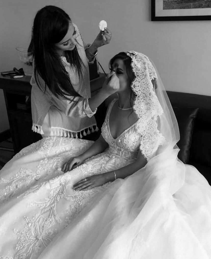 Luma applying makeup to a bride in a lace veil